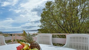 A table with a fruit bowl on a white tablecloth, overlooking a scenic view of the sea and a tree. - Apartment Jelena by Interhome (Karlobag)