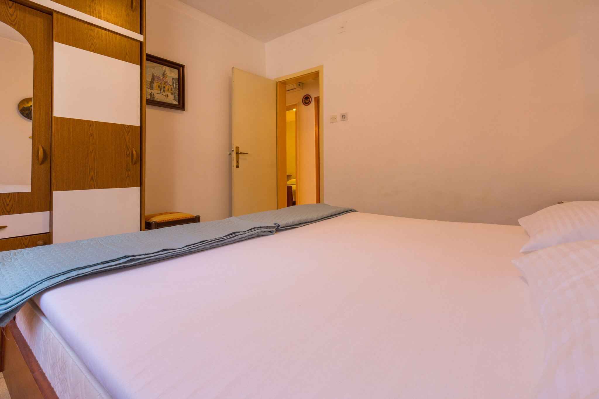 A neatly made bed with a folded blanket, a wooden wardrobe with a mirror, and a door leading to another room.