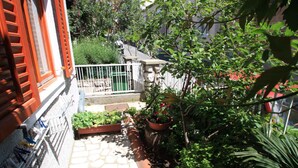 Un cortile con un patio piastrellato, piante in vaso e un recinto bianco.