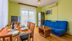 A dining area with a wooden table set for four, a blue sofa, and a television. - Holiday apartment with balcony and air conditioning (Crikvenica)