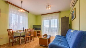A living room with a blue sofa, wooden chairs, a small table, and a television. - Holiday apartment with balcony and air conditioning (Crikvenica)