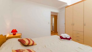Un dormitorio con cama, mesita de noche con lámpara, armario y vistas a un pasillo.