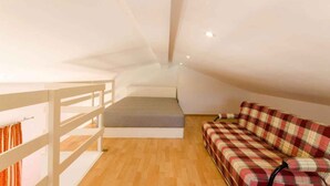 Un dormitorio abuhardillado pequeño y bien iluminado con una cama individual, un sofá y piso de madera.