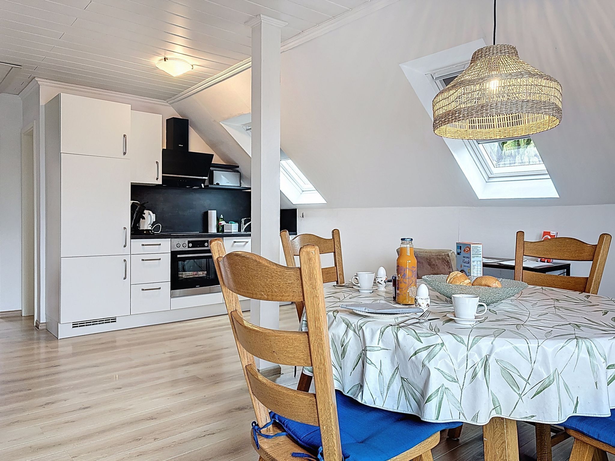 A dining area with a table set for breakfast, a kitchen in the background, and a skylight above.