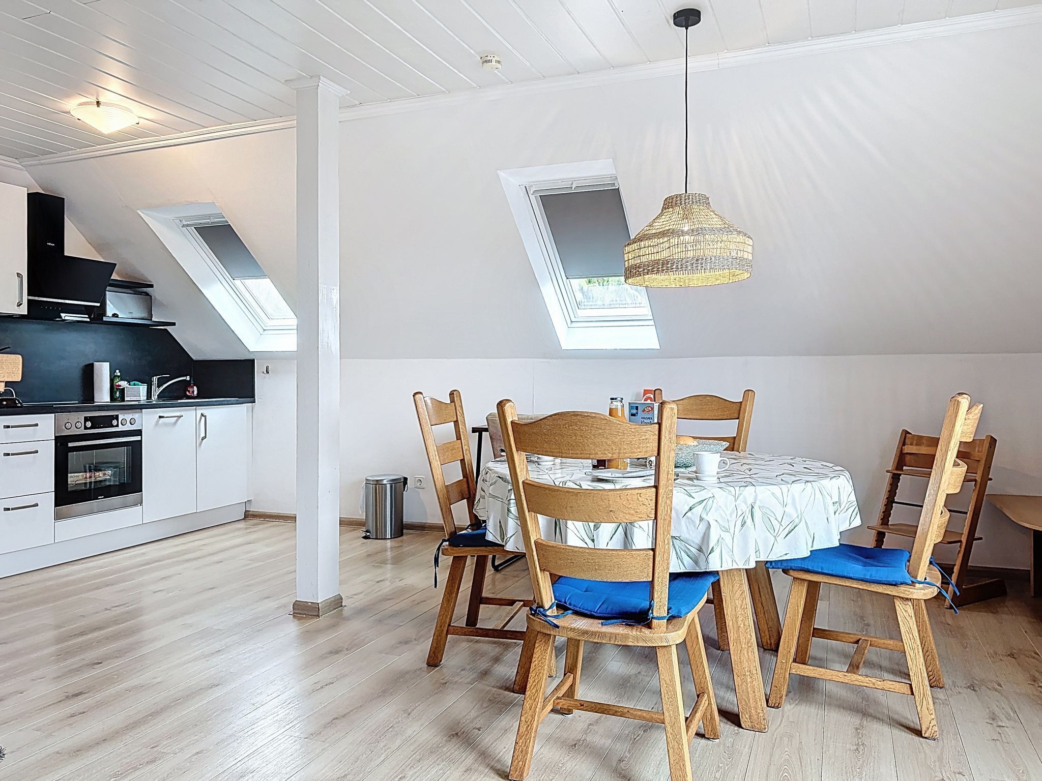 Una cocina moderna con armarios blancos, horno empotrado y comedor con sillas y mesa de madera.