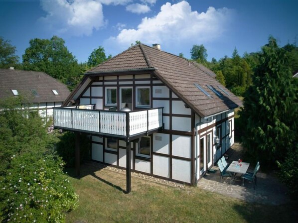 A traditional half-timbered house with a balcony, surrounded by greenery.
