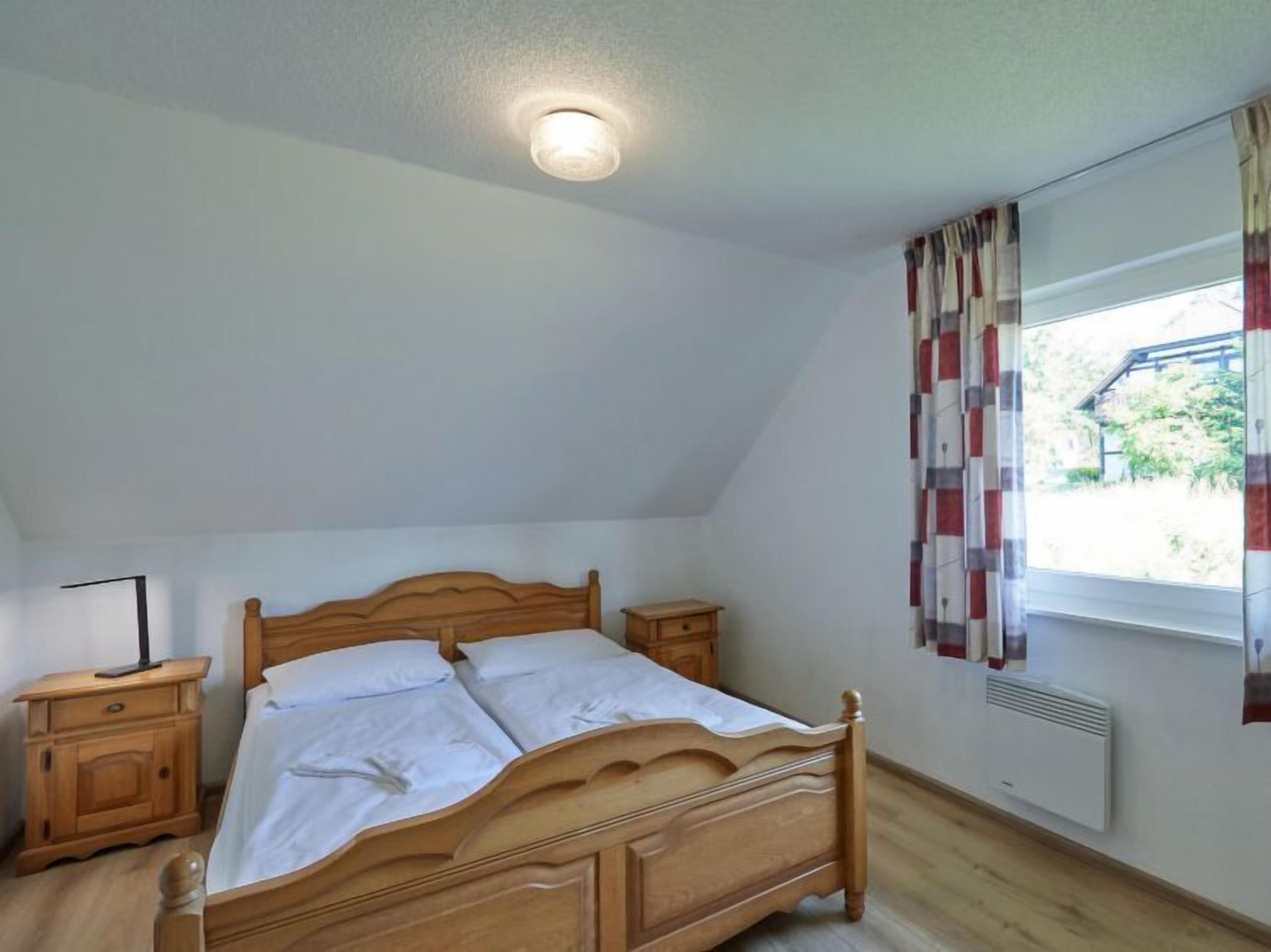 A bedroom with a wooden bed, a nightstand, a window with curtains, and a ceiling light.