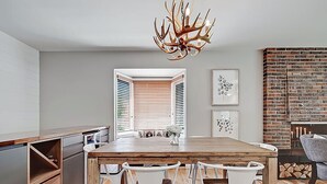 Een moderne keuken met een houten eettafel, witte stoelen en een bijzondere lamp met geweiën.
