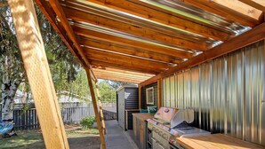 Een buitenkeuken met een barbecue, oven en spoelbak, onder een houten pergola.