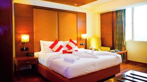 A hotel room with a large bed, a nightstand with a phone, a desk, and a chair. - Fortel (Chennai)