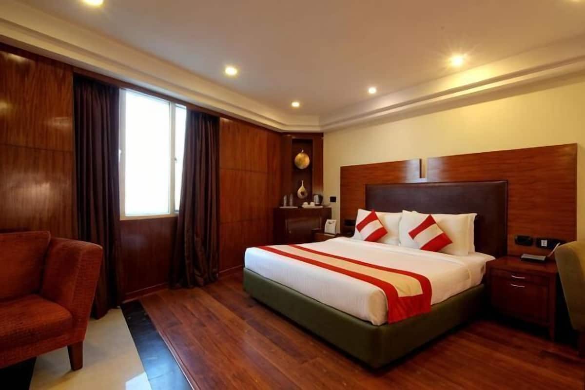 A hotel room with a large bed, wooden flooring, a desk, and a chair.