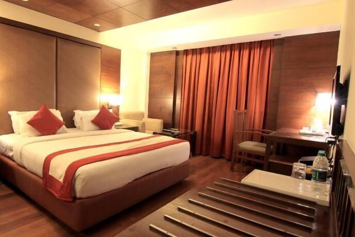 A hotel room with a large bed, a desk, a chair, a TV, and a nightstand with a phone.
