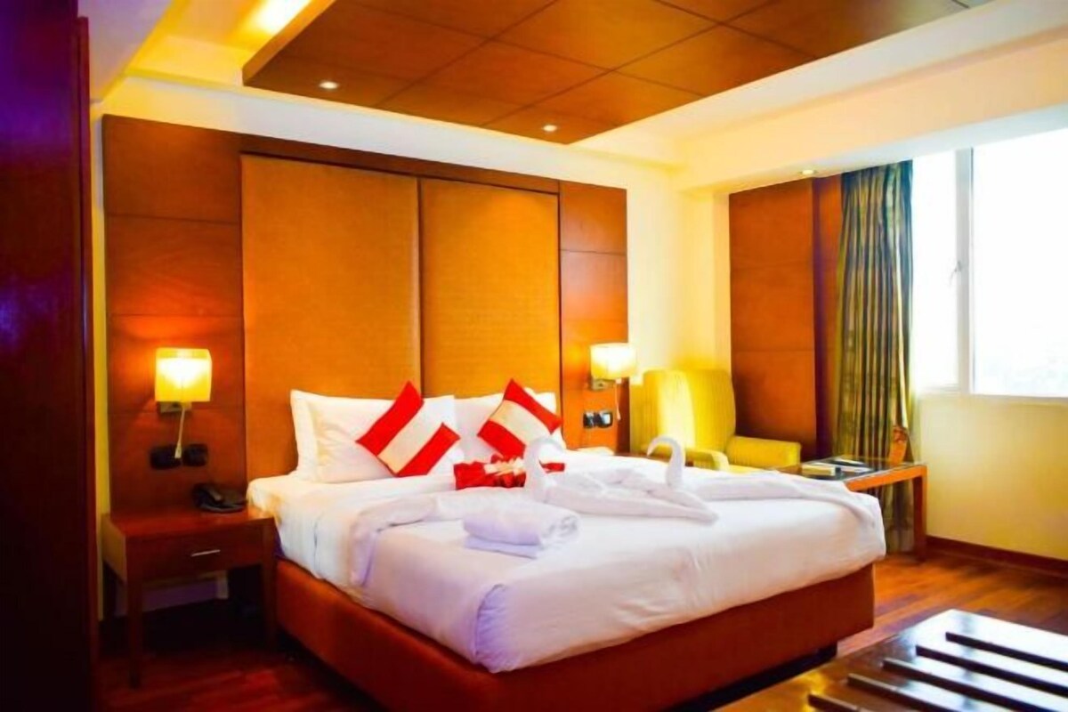 A hotel room with a large bed, bedside tables, a chair, and a window with curtains.