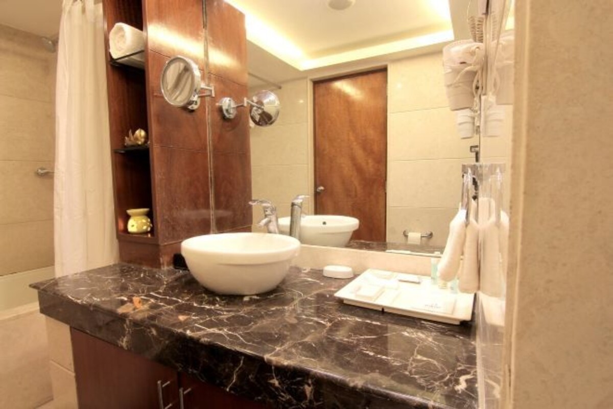 A bathroom with a marble countertop, a large mirror, a sink, a toilet, and a shower curtain.