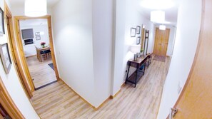 A hallway with wooden flooring, white walls, and a door leading to a room with a bed. - Inverness City Centre Apartment with Elevator (Inverness)