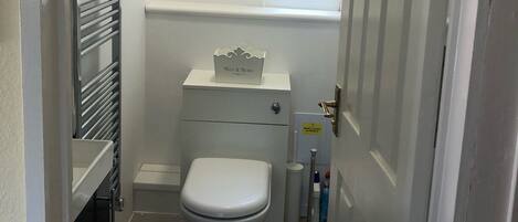 Un baño pequeño con inodoro, una ventana, un radiador y un estante con una caja etiquetada 'Bits & Bobs'.