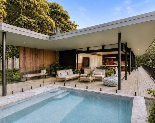Uma área de piscina moderna ao ar livre, com assentos e um terraço coberto.