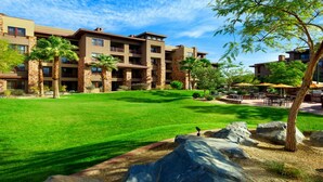 A multi-story hotel with a well-maintained lawn, outdoor seating area, and large rock formations. - Westin Desert Willows (Palm Desert)
