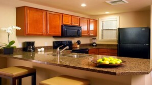 A modern kitchen with granite countertops, wooden cabinets, a black refrigerator, a microwave, and a sink. - Westin Desert Willows (Palm Desert)