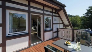 Une terrasse en bois avec une table dressée pour les repas, une porte-fenêtre coulissante donnant sur la cuisine et un balcon doté d’une balustrade.