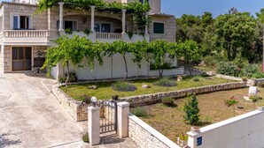 Una casa de dos pisos con fachada de piedra, un balcón y un jardín con diversas plantas y un árbol pequeño.