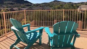Two turquoise Adirondack chairs on a wooden deck with a view of a hilly landscape and houses in the background.