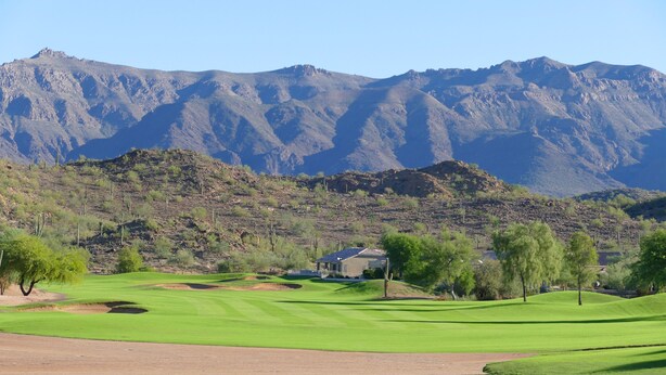 A golf course with a house in the background and mountains.