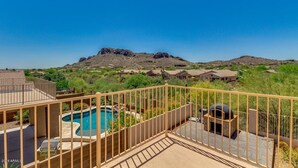 A pool area with a hot tub and barbecue grill, surrounded by a wooden fence, overlooking a mountainous landscape.