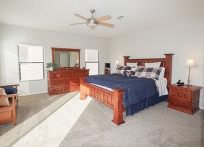 Quarto com cama de madeira, cômoda, mesa de cabeceira, ventoinha no teto e janela com persianas.