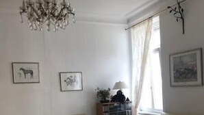 Ein Wohnzimmer mit einem beigen Sofa, einem Glastisch, einer Kristallleuchtre und einem fenster mit Vorhängen.