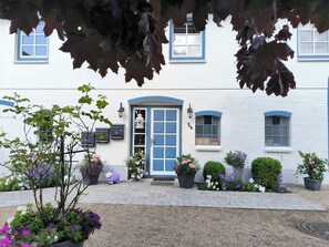 A white building with blue trim and a blue door, surrounded by potted plants and flowers.
