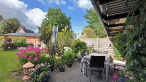 Une terrasse avec une table et des chaises, entourée de plantes et de fleurs en pot.