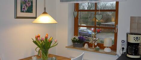 A cozy dining area with a wooden table, a vase of tulips, and a window with a view of parked cars.
