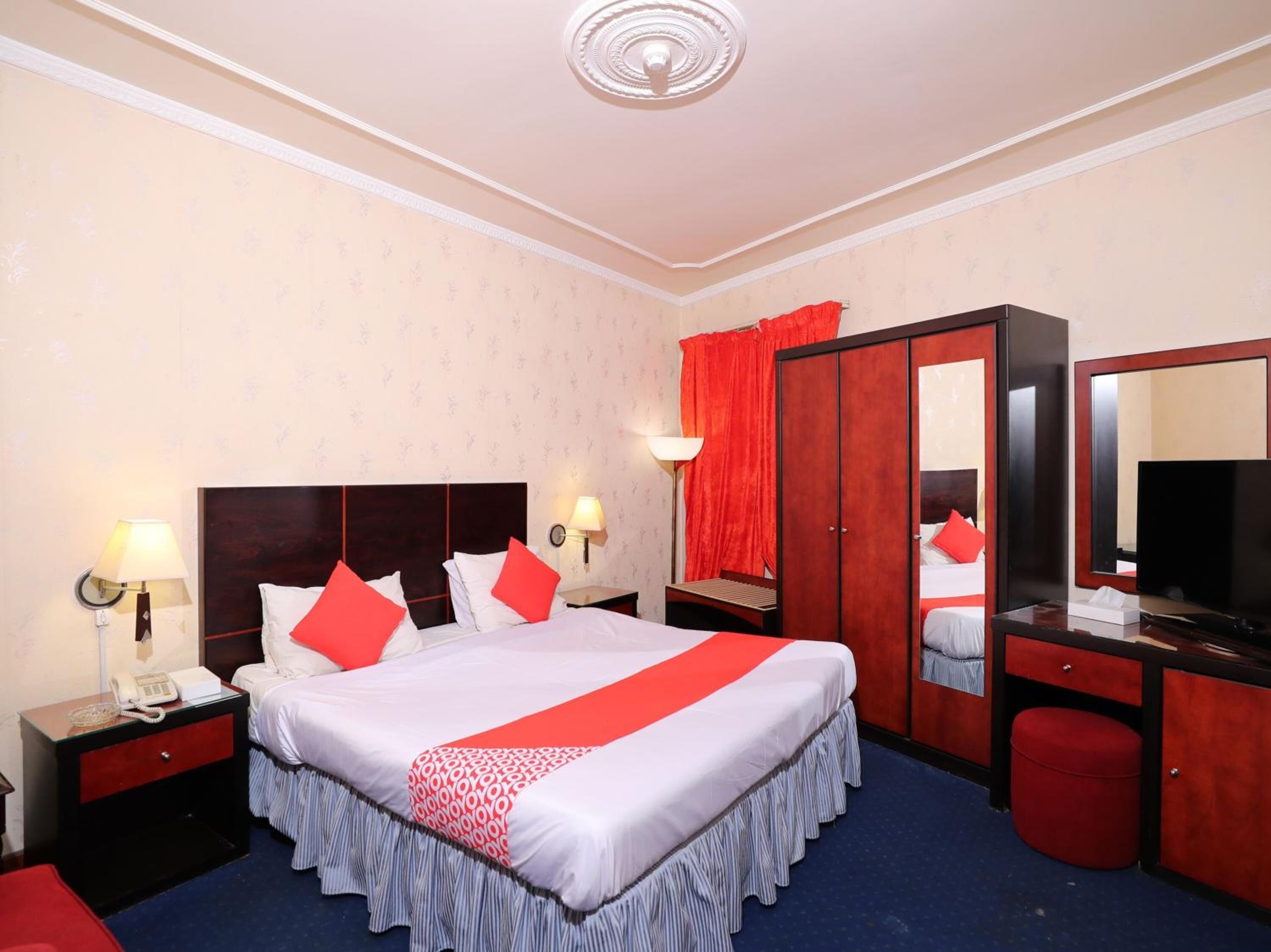 Habitación de hotel con una cama grande, un armario, un escritorio con espejo, un televisor y un teléfono en la mesita de noche.