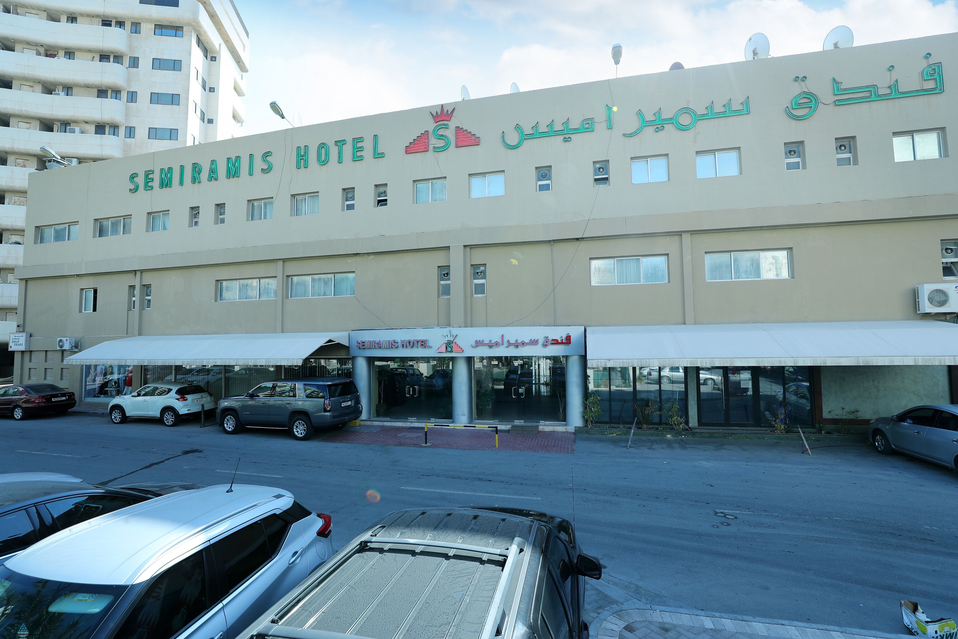 A hotel building with multiple windows and a sign in both English and Arabic.