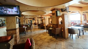 A spacious lobby with a TV mounted on the wall, comfortable seating, and a brick wall with a clock. - OYO 112 Semiramis Hotel (Manama)