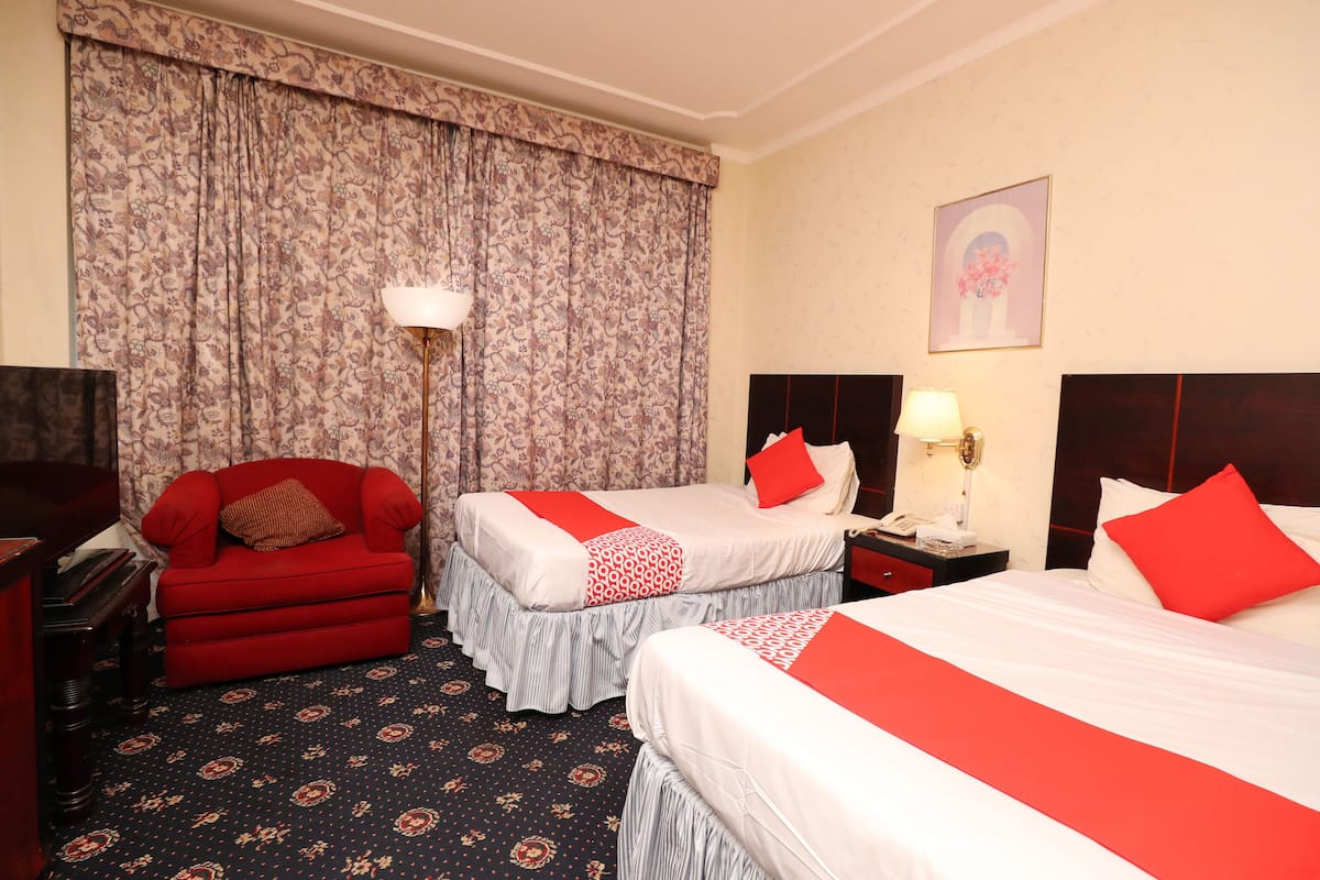 A hotel room with two beds, a red sofa, a piano, and a patterned carpet.