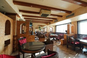 A spacious indoor area with high ceilings, exposed beams, and brick walls. There are multiple seating areas with wicker furniture and cushioned chairs. - OYO 112 Semiramis Hotel (Manama)