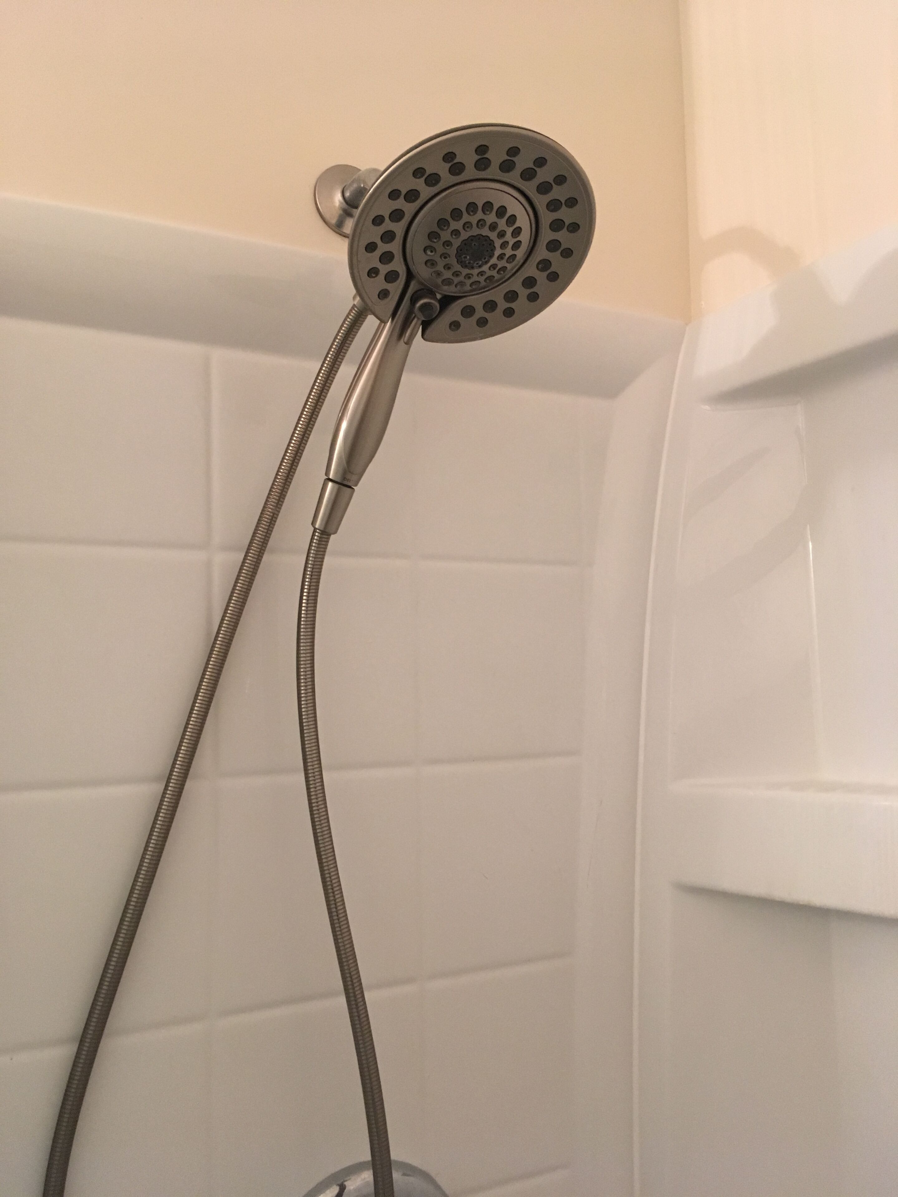 A showerhead with a flexible hose in a bathroom with white tiled walls.