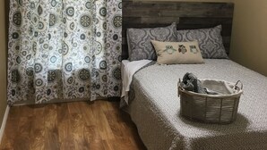 A bedroom with a wooden floor, a bed with patterned bedding, a headboard, and a basket on the bed.