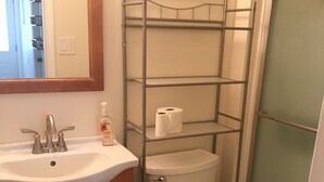 A bathroom with a white sink, wooden cabinets, a toilet, and a metal shelf unit above the toilet.