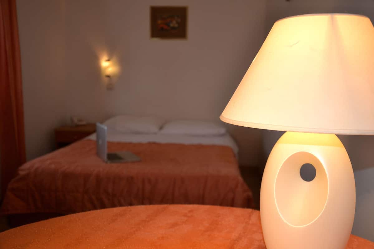 A hotel room with a bed, a bedside table, a lamp, and a wall-mounted light fixture.