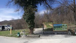 A parking area with a directional sign, a large informational board, and a tree.