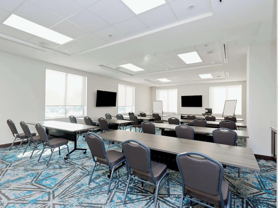 A conference room with a long table, multiple chairs, a flat-screen TV, a whiteboard, and large windows.