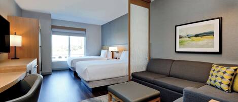 Una habitació d'hotel moderna amb llit, sofà, escriptori i una finestra gran.