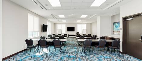 A conference room with a geometric patterned carpet, white walls, and a flat-screen TV on the wall.