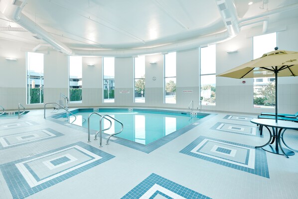 Una piscina interior con señalización clara, una silla de salvavidas y una mesa con sombrilla.