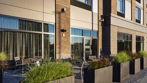 Un bâtiment moderne doté de grandes fenêtres, d’un espace extérieur aménagé pour s’asseoir et de jardinières remplies de verdure.