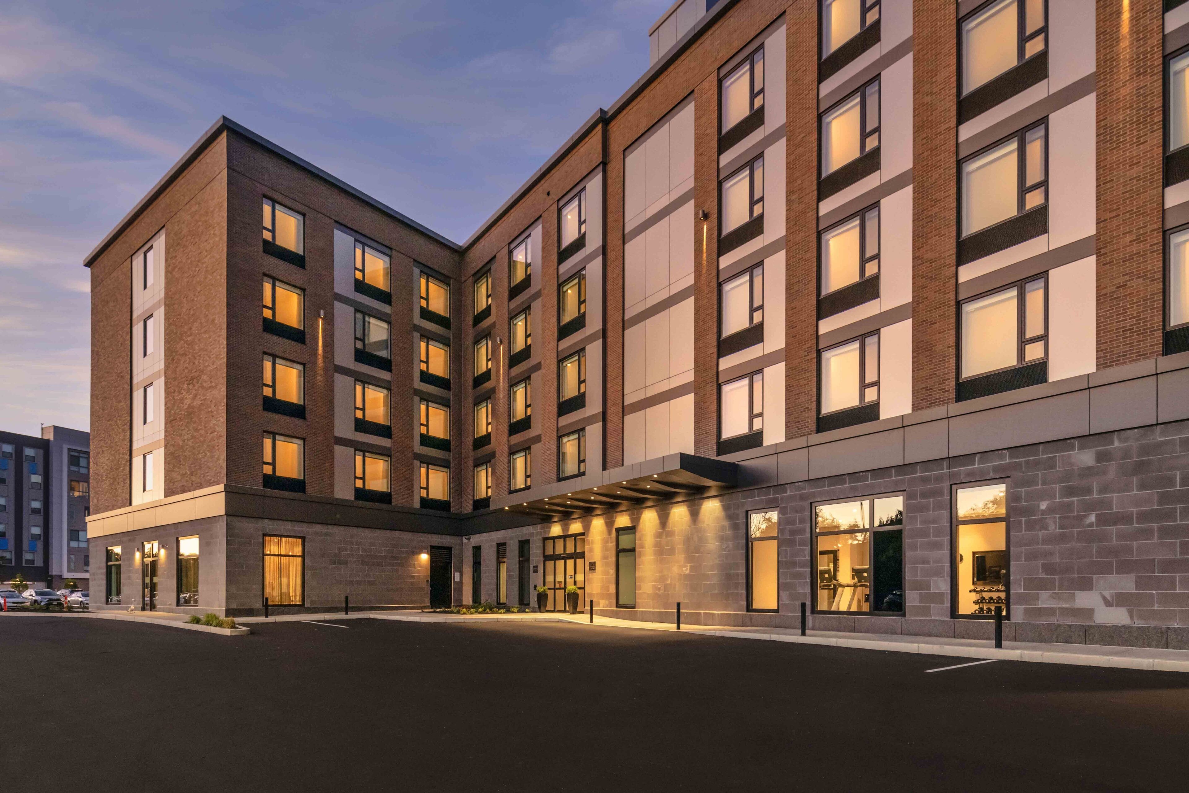A multi-story hotel with a modern design, featuring a courtyard with a covered walkway and a parking area.