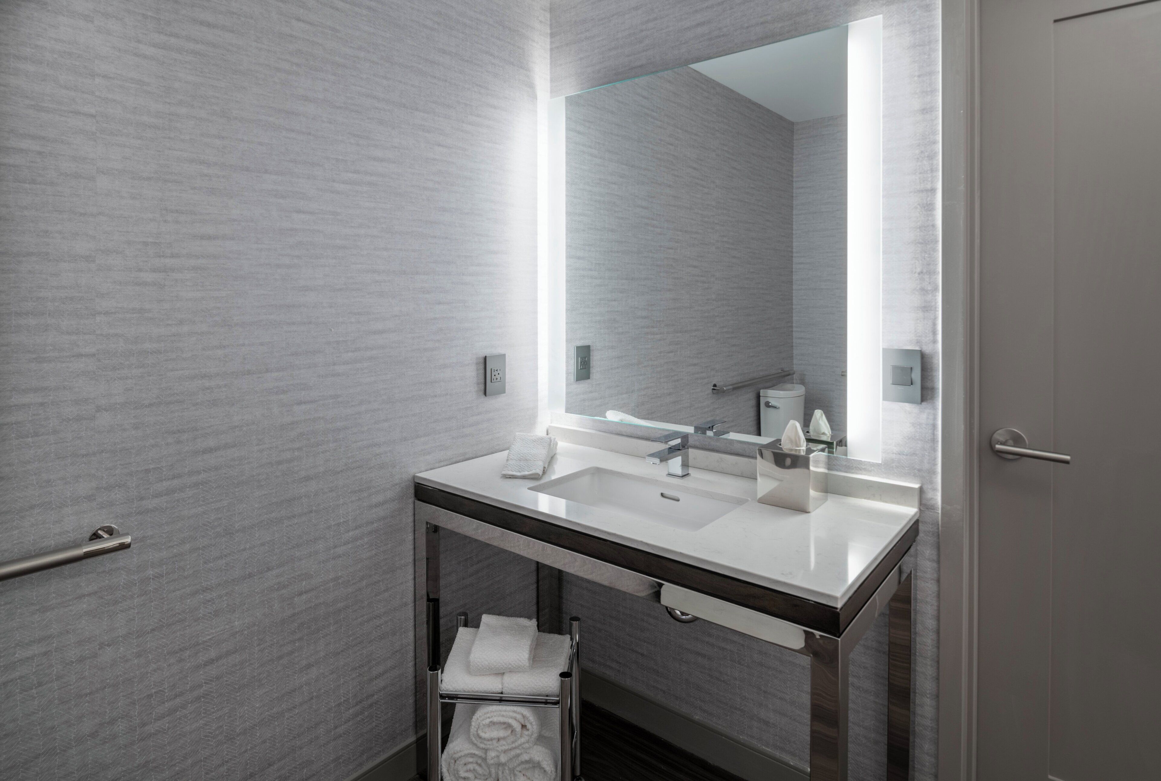 A modern bathroom with a large mirror, a sink, and a towel rack.